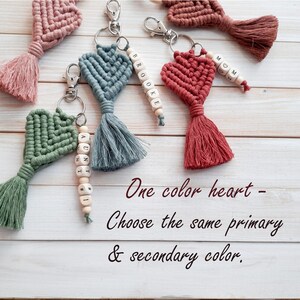 May include: Five crocheted heart keychains with tassels. Each keychain has a different name spelled out on wooden beads. The heart keychains are all the same colour, but the tassels are different colours. The text on the image reads "One colour heart - Choose the same primary & secondary colour."