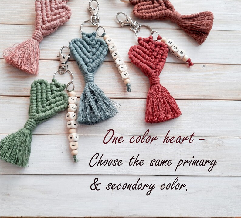 May include: Five crocheted heart keychains with tassels. Each keychain has a different name spelled out on wooden beads. The heart keychains are all the same colour, but the tassels are different colours. The text on the image reads "One colour heart - Choose the same primary & secondary colour."