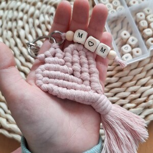 May include: A pink macrame heart keyring with a wooden bead charm that spells "MOM" with a heart bead in between the letters.