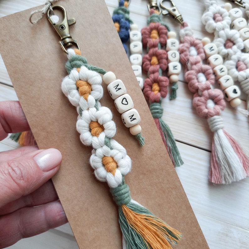 Daisy keychain,  the flowers have white petals and a mustard center, in addition there is also a green color. The word "mom" is made of wooden beads, the letter "o" is replaced by a drawn heart.