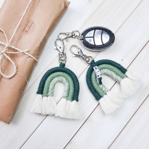 Op de afbeelding: Twee groen-witte regenboog sleutelhangers met witte kwastjes. De sleutelhanger rechts heeft de naam "MIA" in witte letters. Beide sleutelhangers zijn bevestigd aan zilveren sleutelringen.
