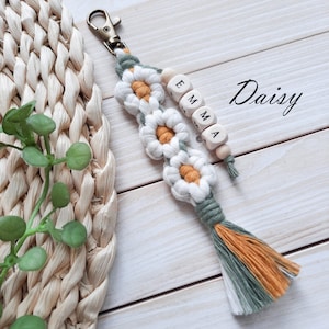 Daisy keychain,  the flowers have white petals and a mustard center, in addition there is also a green color. The name is made with wooden beads.