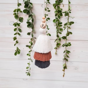 Może przedstawiać: Trójwarstwowa frędzla z białymi, pomarańczowymi i czarnymi warstwami. Frędzla jest zawieszona na drewnianej koralce z literą "P" na niej.