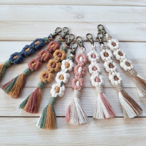 Könnte beinhalten: Ein Set aus sechs bunten Makramee-Schlüsselanhängern mit Blumenmuster. Jeder Schlüsselanhänger hat eine andere Farbkombination aus Blau, Rosa, Grün und Braun.