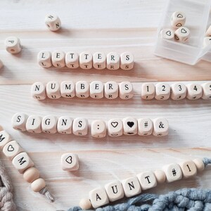 May include: Wooden blocks spelling out the words "LETTERS", "NUMBERS", and "SIGNS". The blocks also include numbers, punctuation marks, and symbols. There are also wooden beads spelling out the words "MOM" and "AUNT".