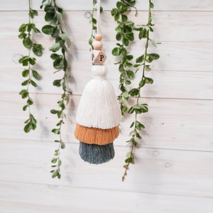 May include: A white, orange, and gray tassel with a wooden bead and a wooden block with the letter "P" on it.
