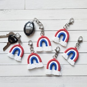 May include: Six red, white and blue rainbow keychains with fringe. The keychains are made of yarn and are attached to silver key rings.