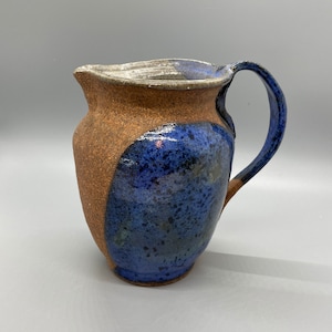 May include: A brown and blue ceramic pitcher with a speckled glaze. The pitcher has a rounded body and a handle.