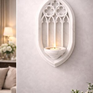 May include: White marble wall sconce with a Gothic arch design. The sconce features a candle holder and a lit candle. The design includes trefoil and lancet arch details. A decorative piece for home decor.