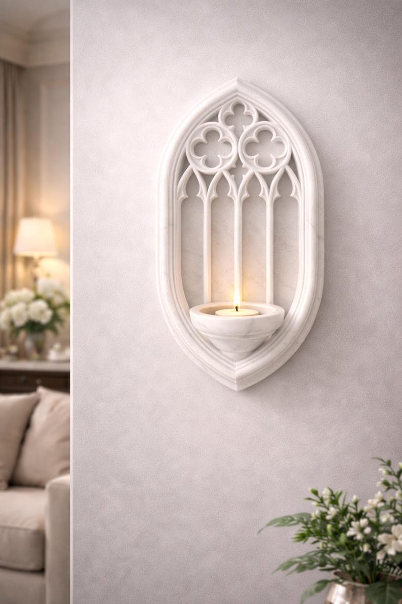 May include: White marble wall sconce with a Gothic arch design. The sconce features a candle holder and a lit candle. The design includes trefoil and lancet arch details. A decorative piece for home decor.