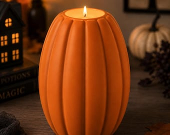 May include: A tall, orange, pumpkin-shaped candle with vertical ridges and a smooth matte finish. The candle is lit, featuring a single flame centered at the top. The wax form is oval and symmetrical, designed to resemble a gourd with deep grooves.