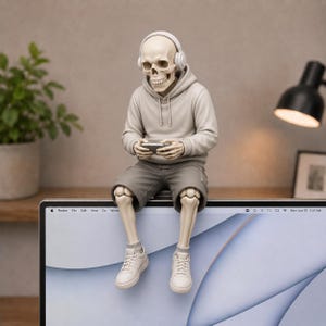 May include: A skeleton figurine wearing a beige hoodie, gray shorts, white sneakers, and white headphones, sitting on the top edge of a computer monitor while holding a small rectangular device in its hands. The figure has a light beige bone finish.