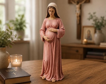 May include: A standing figurine of a pregnant woman wearing a long, flowing dusty pink dress and a light beige head covering. The figure has her hands gently resting on her rounded belly, with a serene expression and visible bare feet at the base.
