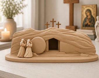 May include: A light tan, monochromatic sculpture depicting an empty tomb with a rolled-away circular stone door. Two figures stand to the left with hands clasped in prayer. Three small wooden crosses are positioned atop the rocky structure.
