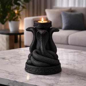 May include: A black candle holder featuring three cobra snake sculptures. The candle holder has a round base with an ornate design and a top that holds a lit candle. The snakes are coiled around the central column.