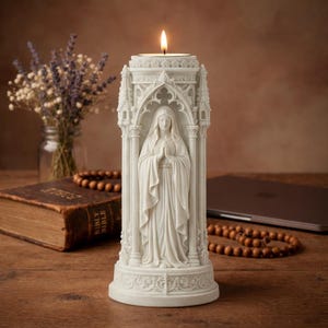 Könnte beinhalten: Ein weißer religiöser Kerzenhalter mit einer Statue einer Frau, die die Hände zum Gebet gefaltet hat. Der Kerzenhalter hat ein verziertes Design im gotischen Stil mit einer brennenden Kerze an der Spitze. Der Kerzenhalter steht auf einer Holzoberfläche.
