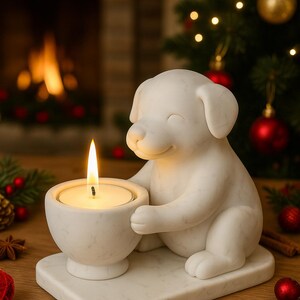 May include: A white marble candle holder shaped like a smiling puppy, holding a lit candle. The candle holder sits on a square base. Christmas decorations, including ornaments and a tree, are in the background.
