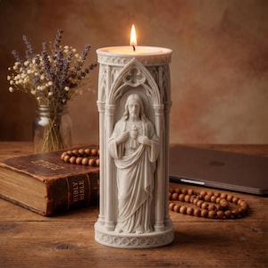 Könnte beinhalten: Eine brennende weiße Kerze in einem dekorativen Halter mit einer geschnitzten Jesusfigur. Der Kerzenhalter hat ein Bogendesign und steht auf einer Holzoberfläche. Ein Blumenstrauß, ein Buch und ein Laptop sind ebenfalls zu sehen.