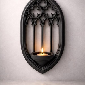 May include: Black gothic-style wall sconce with a lit candle. The sconce has an arched, window-like design with decorative trefoil details. The candle sits in a small, round holder, casting a warm glow.