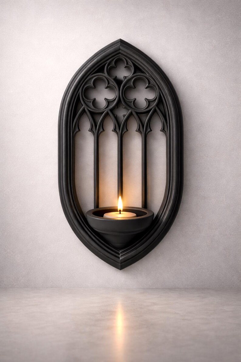 May include: Black gothic-style wall sconce with a lit candle. The sconce has an arched, window-like design with decorative trefoil details. The candle sits in a small, round holder, casting a warm glow.