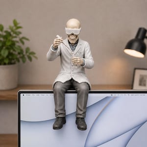 May include: A skeleton figurine wearing white safety goggles, a white lab coat, and gray trousers. The figure is seated, holding a clear pipette and a test tube. The skeleton has a neutral expression and is positioned on the top edge of a computer monitor.