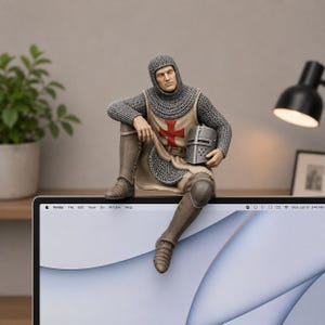 May include: A figurine of a medieval knight wearing a chainmail coif and tunic with a red cross emblem on the chest. The knight is seated, holding a grey metal helmet in one hand, and is dressed in brown greaves and boots over chainmail armor.
