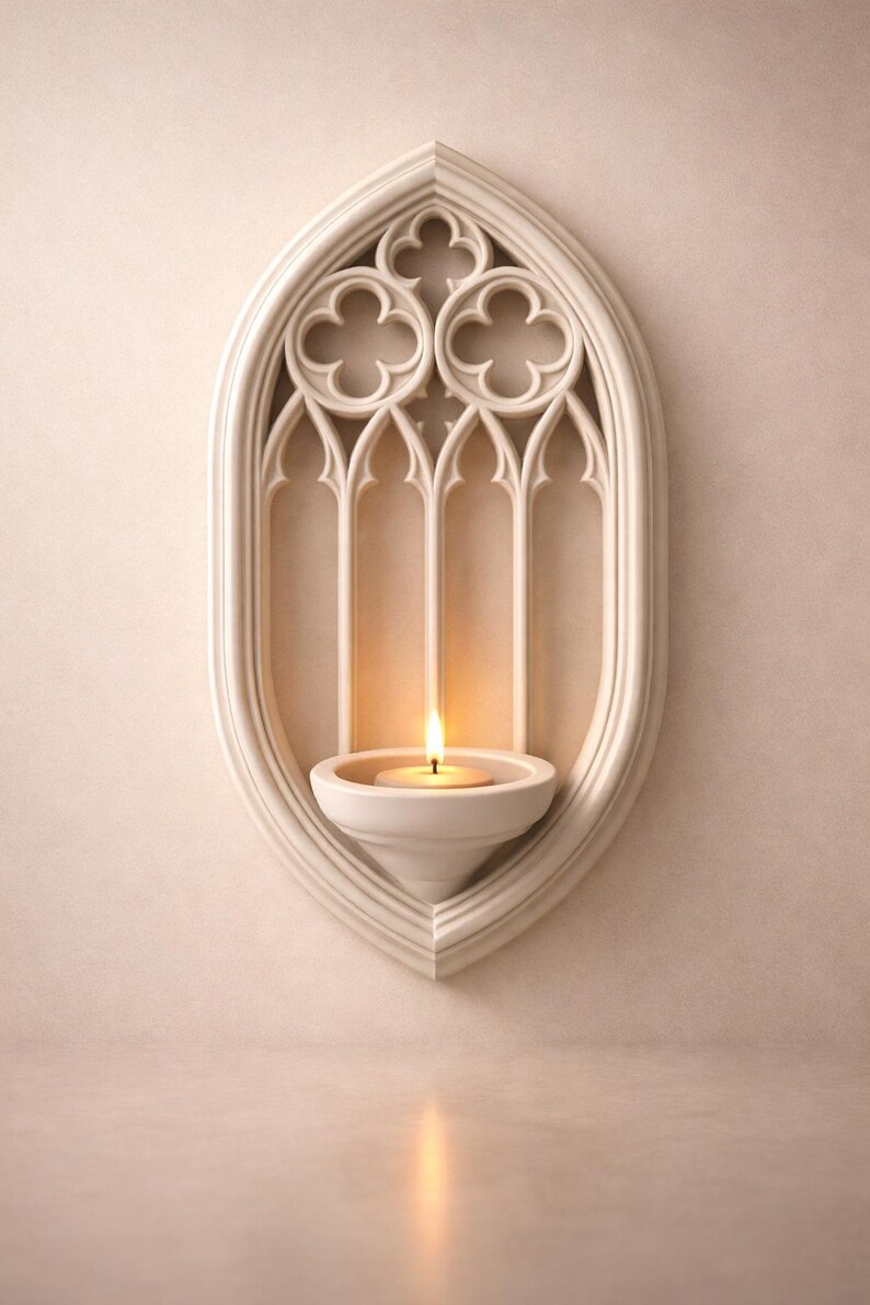 May include: A white, gothic-style wall sconce with a lit candle. The sconce has an arched design with decorative cutouts and a small, round candle holder. The candle flame casts a warm glow, creating a serene ambiance.