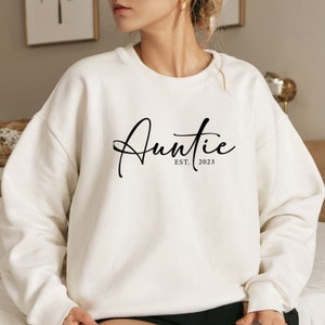 May include: White sweatshirt with black text that reads "Auntie Est. 2023".