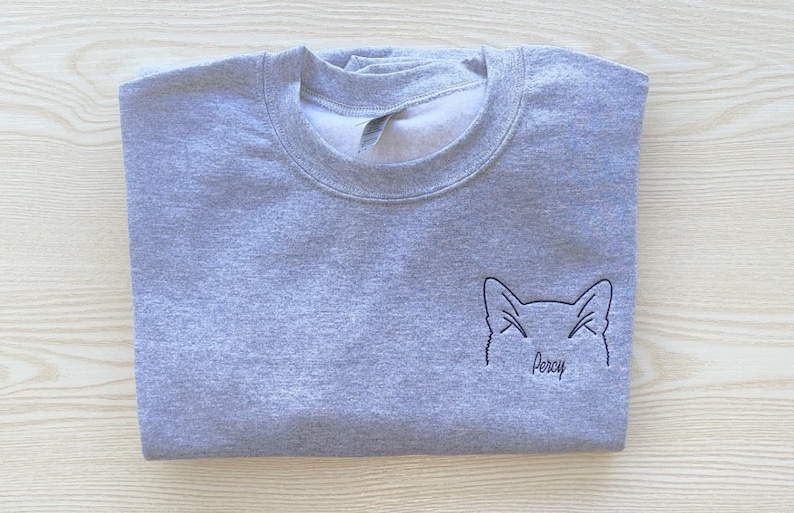 May include: Gray sweatshirt with a black embroidered outline of a cat's face and the name "Percy" underneath.