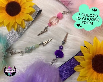 May include: Seven colors of fuzzy hair clips with silver clips and charms. The clips are displayed on a white background with glitter fabric and faux fur.