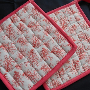 May include: Two red and white quilted pot holders with a coral reef design. The pot holders have a pink border.
