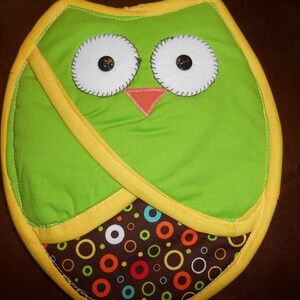 May include: Green owl-shaped pot holder with yellow trim and a brown and white polka dot pattern on the bottom.