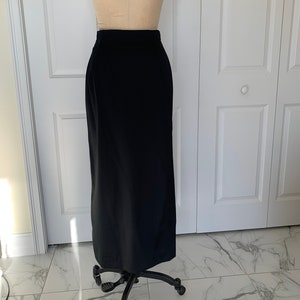 May include: A long black skirt with a high waistline. The skirt is made of a smooth, wrinkle-resistant fabric.