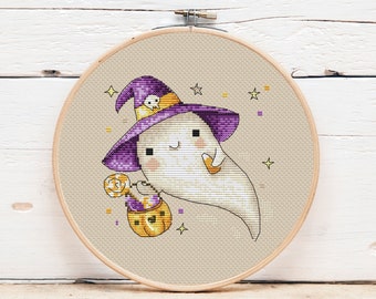 Puede incluir: Bordado de punto de cruz de un fantasma amigable con un sombrero de bruja morado con una calavera, sosteniendo un cubo de caramelos con forma de calabaza y una piruleta. El fantasma tiene mejillas rosadas y está rodeado de estrellas. El bordado está en un aro de madera.