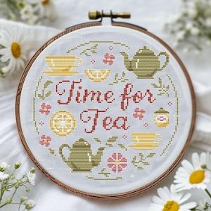Pode incluir: Um bastidor de bordado em ponto cruz com a frase "Time for Tea" em vermelho. O design inclui xícaras de chá amarelas, bules, fatias de limão e flores cor-de-rosa sobre um fundo azul claro. O bastidor de madeira é visível.