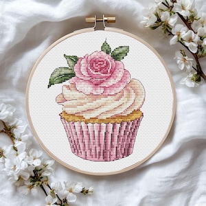 Op de afbeelding: Een roze en witte cupcake met een roze roos erop. De cupcake zit in een roze en witte papieren vormpje en staat op een witte achtergrond.
