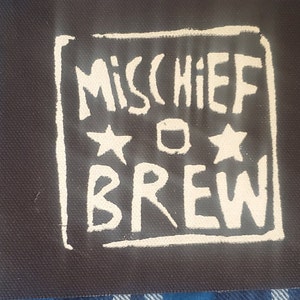 May include: A black fabric patch with white lettering that reads "Mischief Brew" with two white stars and a circle in between the words.