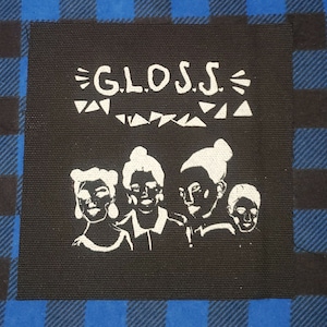 May include: Black square patch with white text and illustration. The text reads "G.L.O.S.S." above a stylized image of four figures. The patch is set against a blue and black plaid background.
