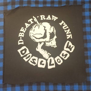 May include: Black and white embroidered patch with a skull holding a microphone and the text "D-BEAT RAW PUNK DISCLOSE"