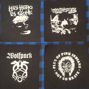 May include: Four black fabric patches with white designs. The top left patch says "His Hero Is Gone". The top right patch says "Warzone". The bottom left patch says "Wolfpack" with a wolf head design. The bottom right patch says "Flux of Pink Indians - Not So Brave".