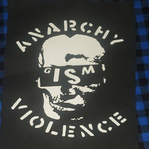 May include: Black and white patch with the words "Anarchy Is Violence" in a circle around a stylized face with the word "ISM" covering the eyes.