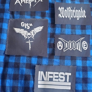 May include: Five black fabric patches with white lettering. The patches feature the band names "Amebix", "Wolfbrigade", "GISM", "A.D.O.M.E", and "INFEST".