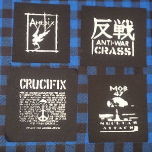 May include: Four black fabric patches with white text and graphics. The patches feature the band names Amebix, Crass, Crucifx, and Mob 47. The patches are on a blue and white checkered background.