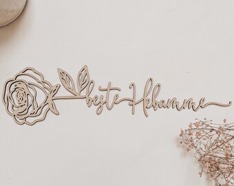 Puede incluir: Un letrero de madera con un diseño de rosa y hojas y el texto "beste Hebamme" en cursiva.