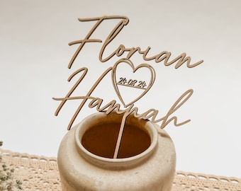 May include: Wooden wedding cake topper with the names "Florian" and "Hannah" and a heart with the date "24-08-24" in cursive script.