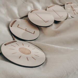 Peut inclure: Une banni&egrave;re en bois avec les lettres "ELA" et un motif soleil. La banni&egrave;re est en bois naturel et a un aspect rustique.