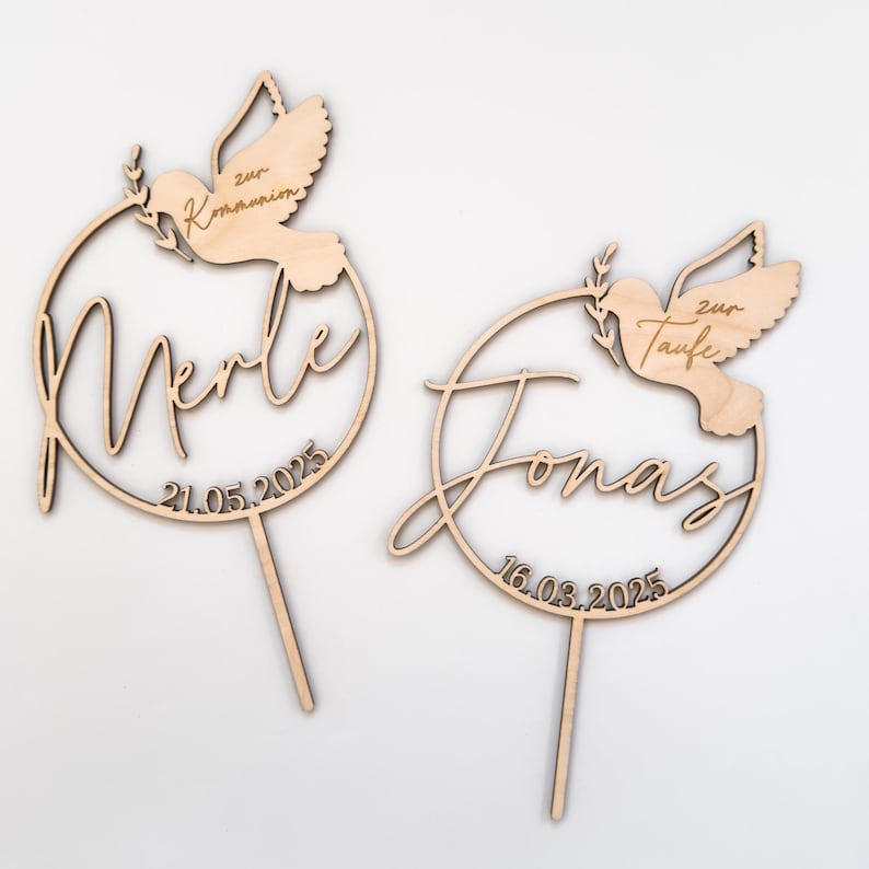 May include: Two wooden cake toppers with doves and a circle design. The first topper says "Merle" with the date "21.05.2025" and the text "zur Kommunion". The second topper says "Jonas" with the date "16.03.2025" and the text "zur Taufe".