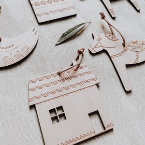 May include: A set of five wooden ornaments, each with a different design. The ornaments are in the shape of a house, a horse, a bird, and two geometric shapes. The ornaments are all painted in a light brown color and have intricate details.