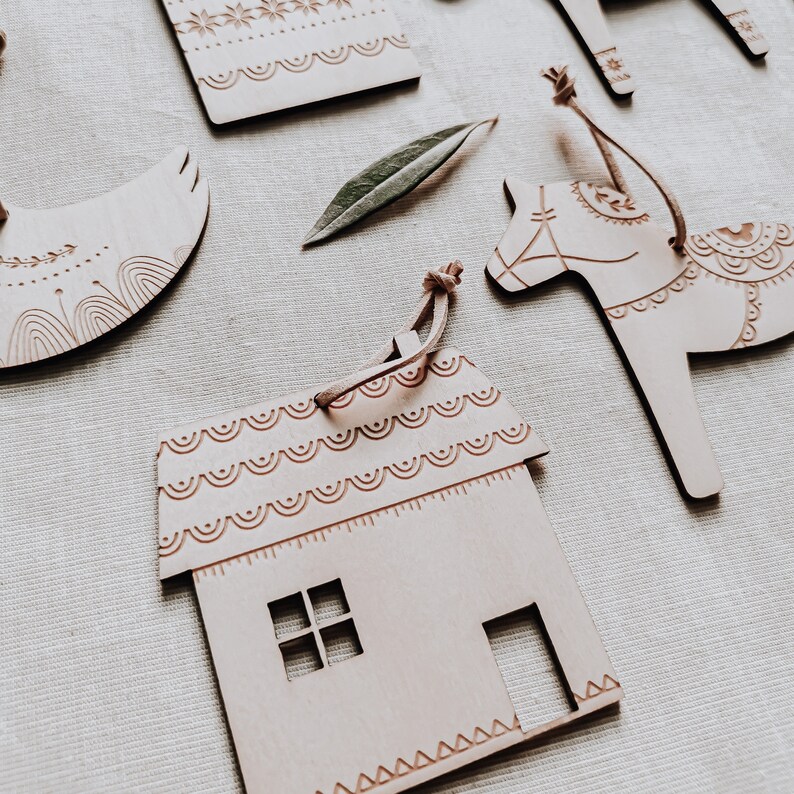 May include: A set of five wooden ornaments, each with a different design. The ornaments are in the shape of a house, a horse, a bird, and two geometric shapes. The ornaments are all painted in a light brown color and have intricate details.