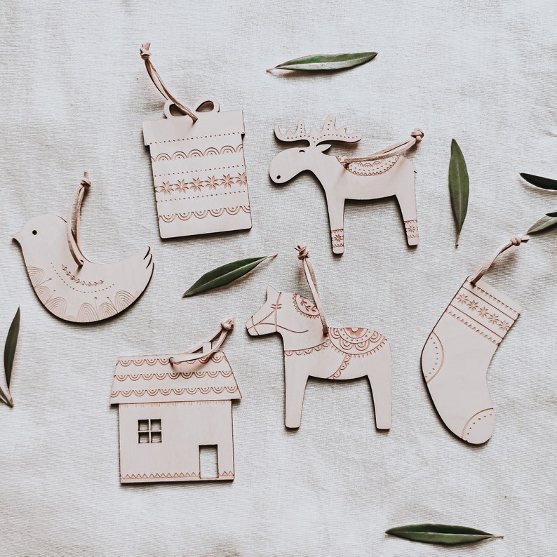 May include: Set of six wooden Christmas ornaments featuring a bird, house, gift box, reindeer, horse, and stocking. Each ornament is painted in a light brown color with intricate details and patterns.